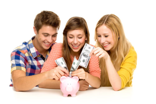 A group of teens saving money by putting dollars into a piggy bank.