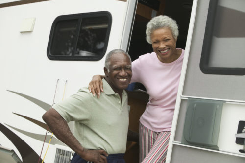 A smiling couple stands outside of their mobile home.