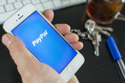 A hand holding up a smartphone, displaying the PayPal app.