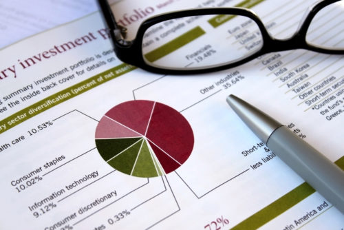 Eyeglasses and a pen sit on top of an investment portfolio.