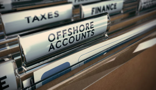 An open file cabinet drawer with many files in it separated by sections labeled "taxes," "finance," and"offshore accounts."