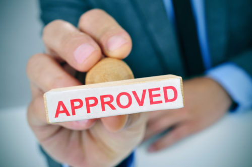 A mortgage loan officer holding up a rubber stamp displaying the word "approved."