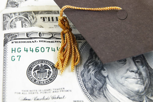 A graduation cap sitting on top of a 100 dollar bill and a 1 dollar bill, alluding to the amount of money it takes for a college education.