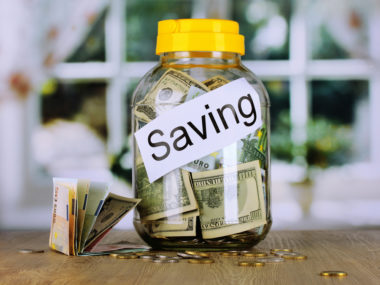 A jar marked "savings" with money in it sitting on a table.