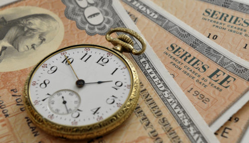 An image of a pocket watch sitting on top of a series of savings bonds.