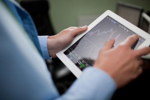An over-the-shoulder view of a businessman looking at a financial graph on a tablet.