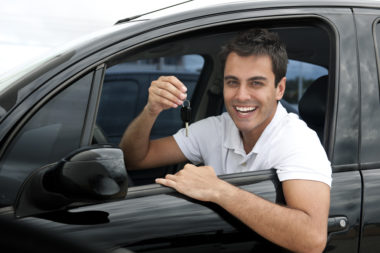 A man holds his car keys out the window of his car while smiling.