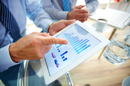 A man pointing a tablet which shows investment income figures and graphs.