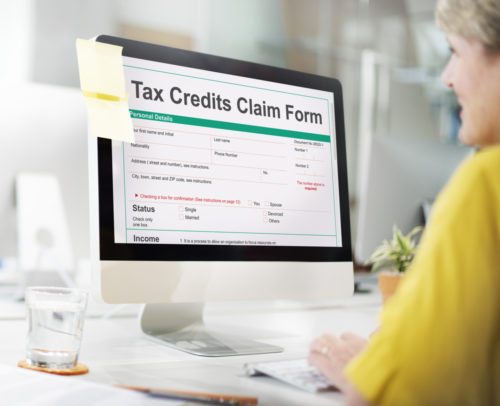 A woman sits at a computer with a screen that displays a tax credits claim form website.