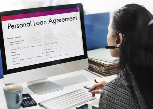 A woman sits at a computer with a screen that reads "personal loan agreement."