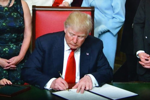 President Donald Trump signing orders at a desk.