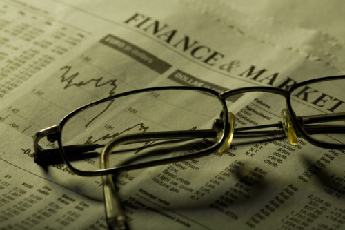 Eyeglasses sit on top of the finance and market page of a newspaper, which is showing a graph that is trending downwards.