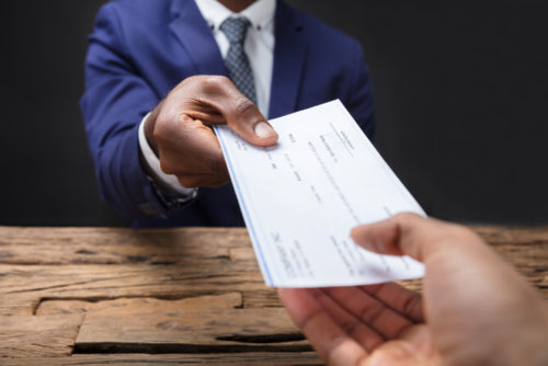 A man in a suit receiving a check over a wooden table.