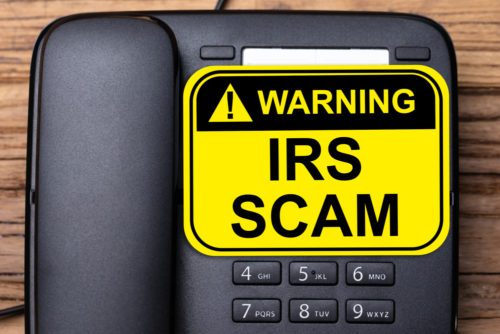 A telephone with a yellow warning sign over it that reads "IRS Scam."
