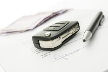 Car keys, cash, and a pen sit on top of a signed car loan agreement.