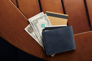 A wallet sitting on top of both cash and a credit card.