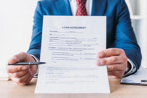 A loan officer holds up a loan agreement contract prompting the viewer to sign with a pen.