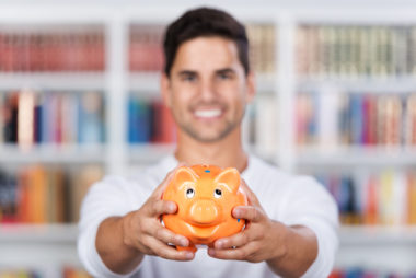 A college student holding up a piggie bank for savings.