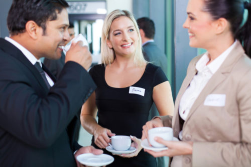 Businessmen and women networking in an office while drinking coffee.