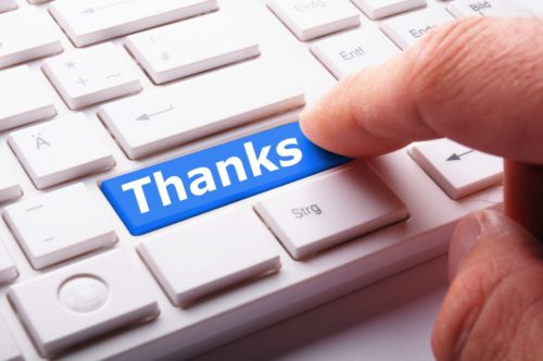 A finger hitting a blue key that says "thanks" on a keyboard of otherwise white keys.