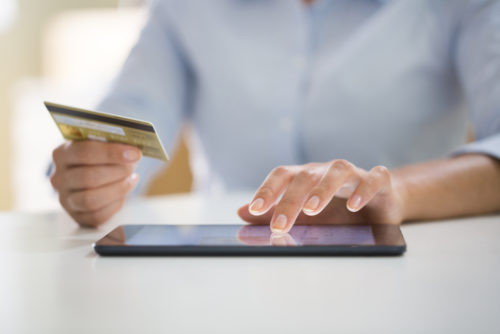 A person paying bills online via a tablet while holding a credit card in their hand.