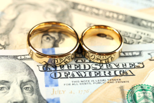 Two gold wedding rings sit on top of American dollar bills.