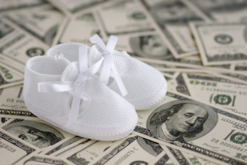 A pair of baby shoes sitting on top of a pile of money.