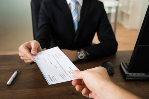 A person handing a check to a clerk behind a desk with a laptop on it.