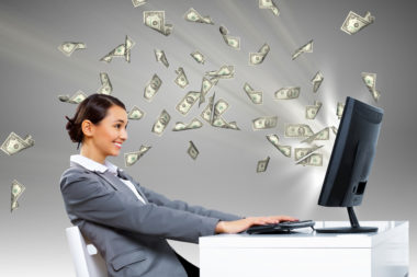 A woman sitting at a computer with dollar bills flying out of the screen.