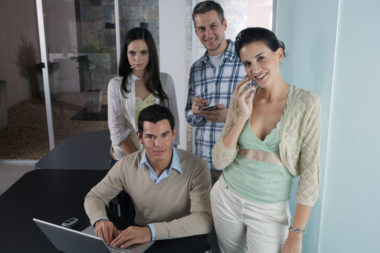 A group of employees standing in their office, all wearing different attire.