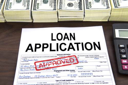 A bank loan application stamped "Approved" and surrounded by cash and a calculator