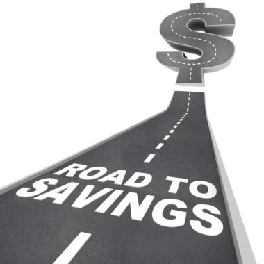 An asphalt road labeled "road to savings" stretches toward the horizon where it changes shape into a dollar sign