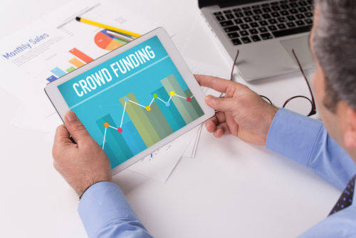 A man sitting at a table while reading a tablet that reads "crowdfunding" on the screen.