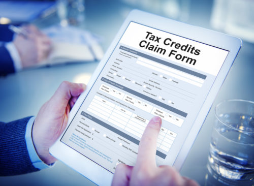 A businessman holds a tablet that reads "tax credits claim form" on the screen.