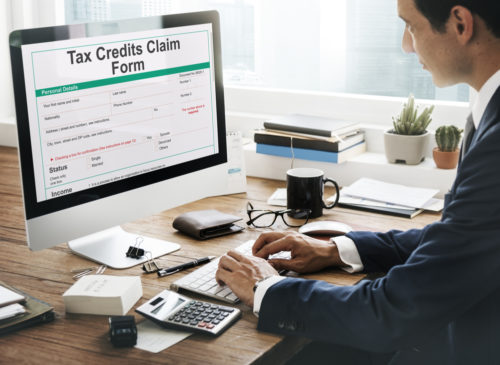 A man typing on a computer that shows a "tax credits claim form" screen.