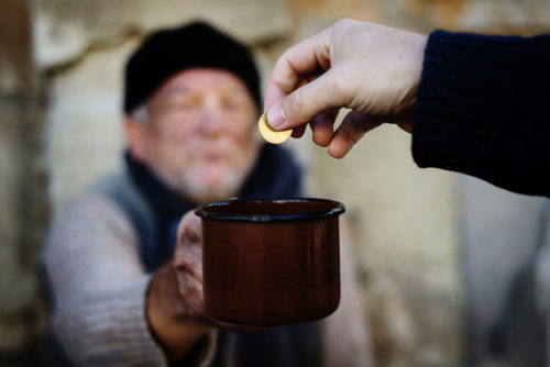 A homeless man receiving one coin in a cup during a recession.
