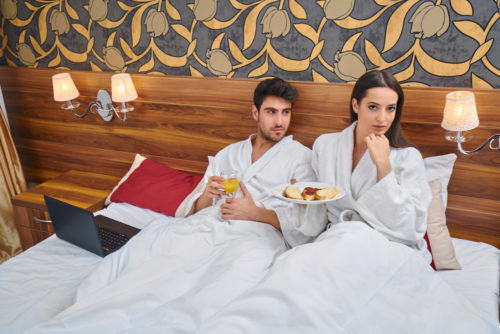 A couple having breakfast in bed in a hotel room while on a weekend getaway.
