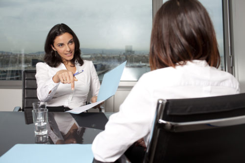 An employer interviews a woman across the desk from her.