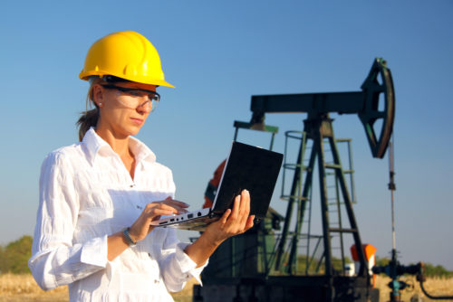 A petroleum engineer working on her laptop in an oil field.