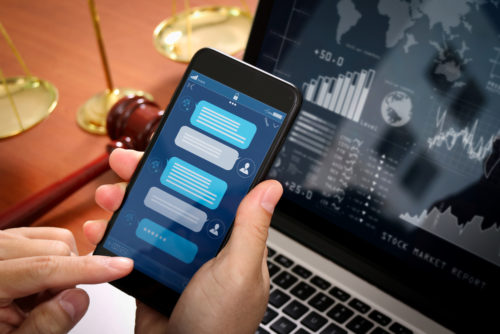 A man sitting at a desk with investment graphs and figures on his laptop, holding a smartphone accessing a robo-advisor.