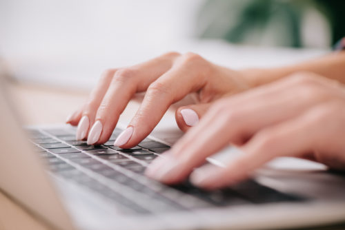 A closeup of a woman's hands typing a farewell email on her laptop.