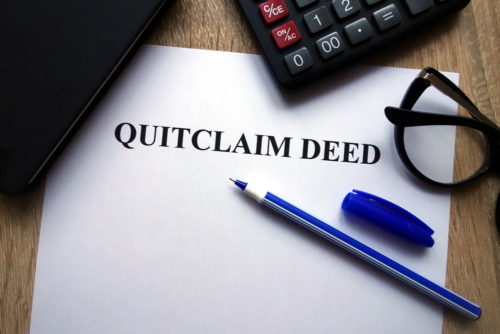 A pen, calculator, and eyeglasses sit on top of a quitclaim deed on a desk.