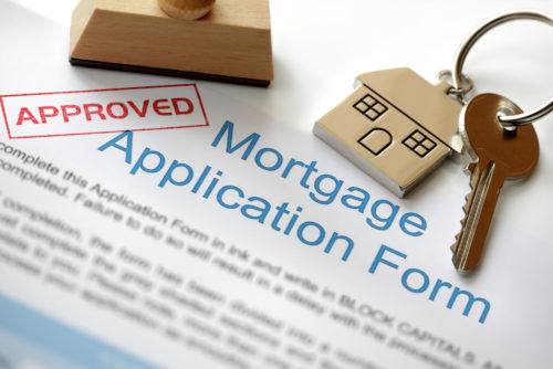 A set of keys sit on top of a mortgage application form rubber stamped "approved."
