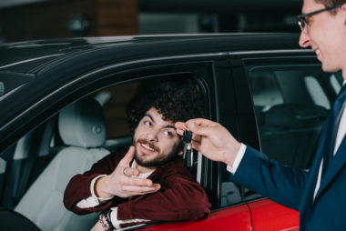 A student receiving the keys to the car he just bought from a car salesman.