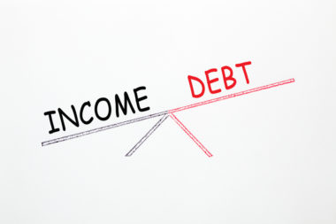A scale balances the words income and debt, with income being heavier than debt.