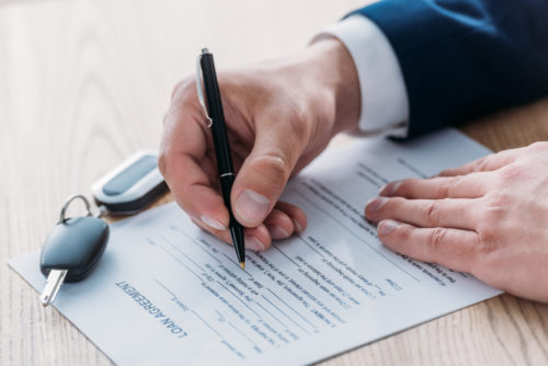 Keys sit on top of a car loan document that is being signed by a man.