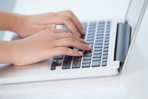 A close up of a woman's hands typing a cover letter on her laptop.