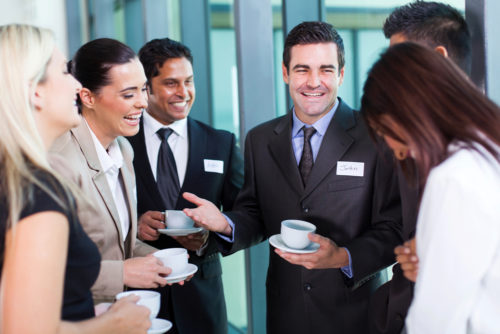 A group of business men and women all gathered around, drinking coffee and networking.