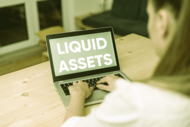 A woman types on a laptop with a screen that reads "liquid assets."