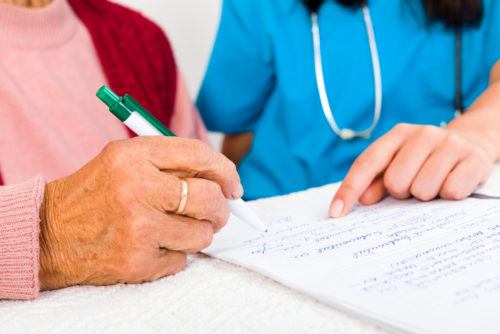 A woman with scrubs and a stethoscope on points to a hospital bill payment plan for another woman to sign.